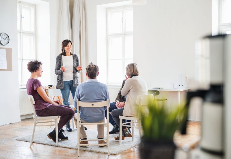 A woman talking to other people during group therapy. A senior woman standing and talking to other people during group therapy.